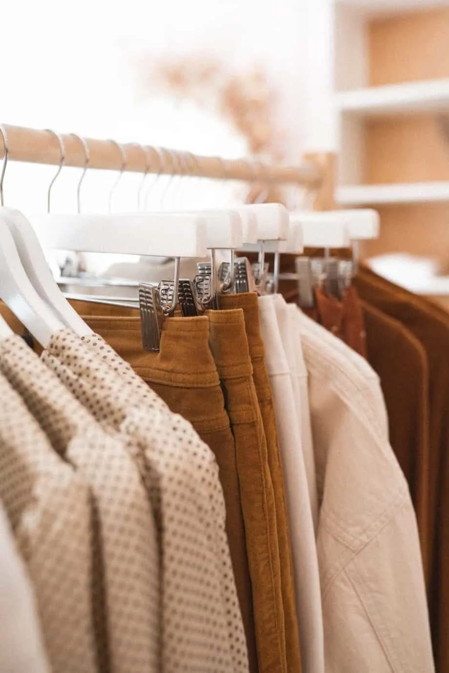 Inside of a wardrobe with tan colored clothes hanging on a rack