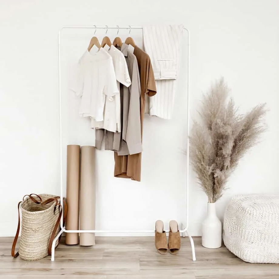 A minimalist tan style collection of clothes hanging on a white rack with a bag next to it