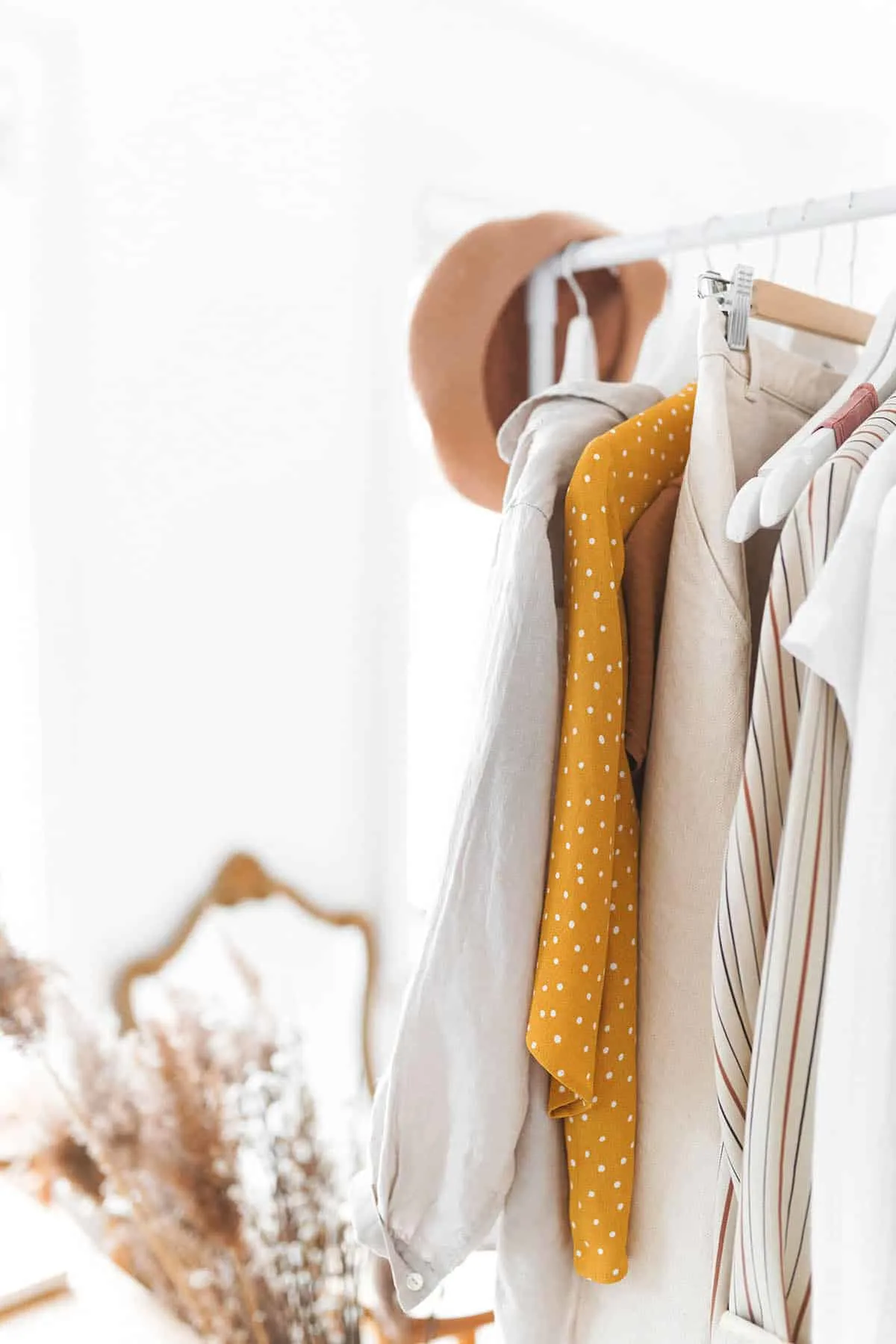 A minimalist wardrobe showing a collection of clothes hanging on a rack and a hat