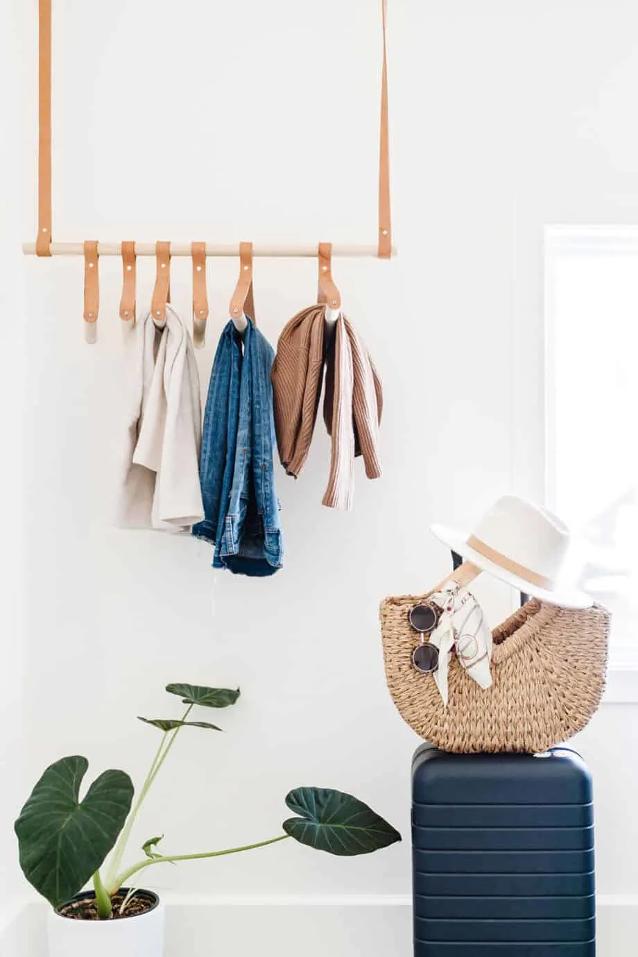 A minimalist display of clothes haning on racks with a bag on a seat and a small plant underneath